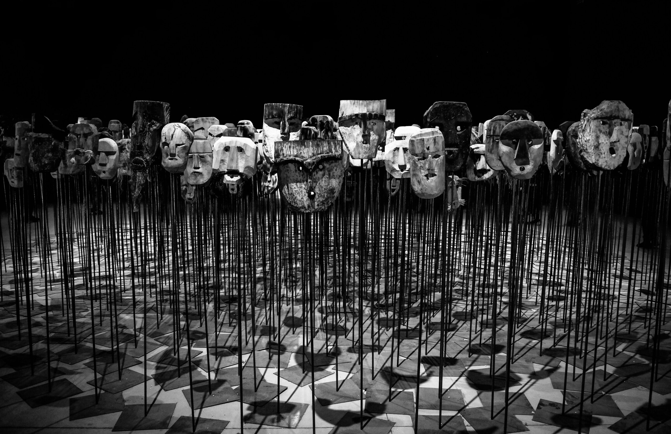 An artistic display of wooden masks on poles, set in a dimly lit theater.